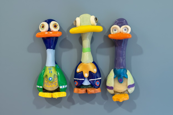 Three colorful duck-shaped figurines with different colored beaks on a reflective surface.