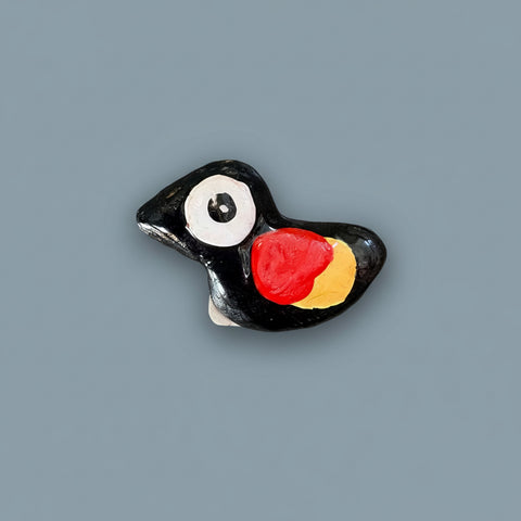 Decorative bird-shaped magnet with black, red, and yellow colors on a gray surface.